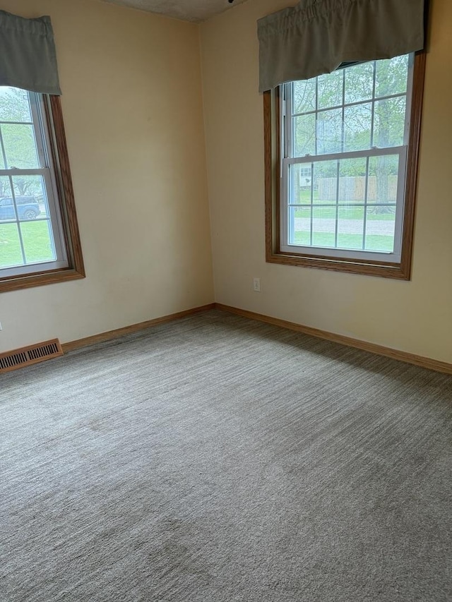 empty room featuring baseboards, a wealth of natural light, carpet flooring, and visible vents