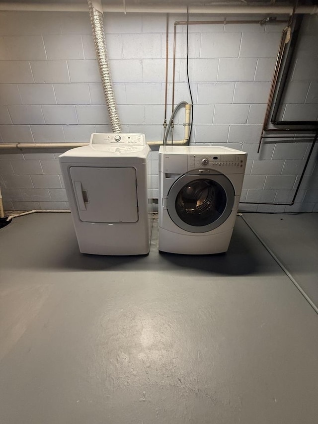 washroom featuring concrete block wall, laundry area, and washing machine and dryer