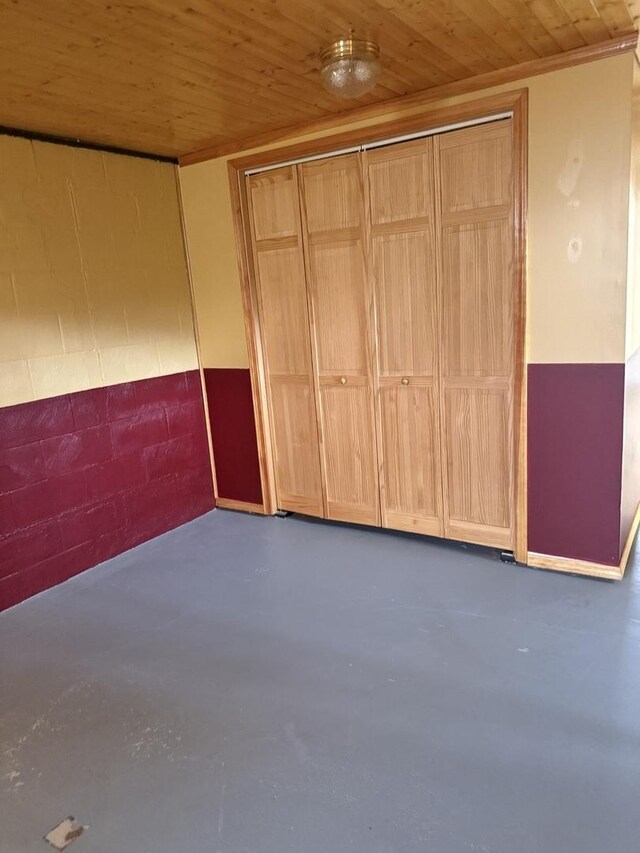 unfurnished bedroom with concrete block wall, wooden ceiling, a closet, and finished concrete floors