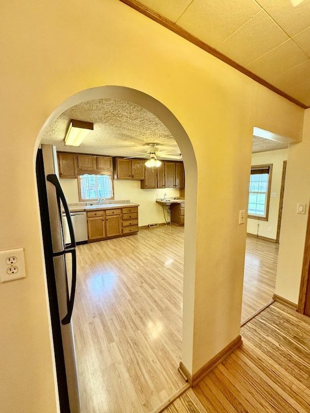 kitchen with arched walkways, a sink, stainless steel appliances, and light wood-style floors