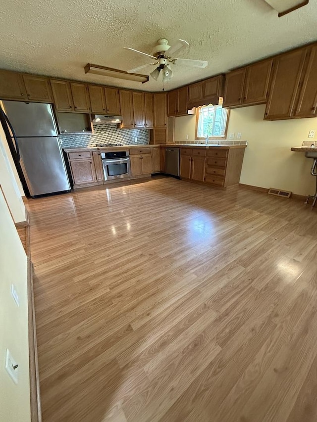 kitchen featuring a textured ceiling, visible vents, brown cabinets, stainless steel appliances, and light wood-style flooring