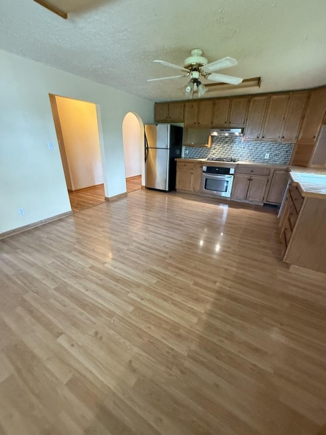 kitchen featuring a ceiling fan, appliances with stainless steel finishes, arched walkways, light wood-style floors, and under cabinet range hood