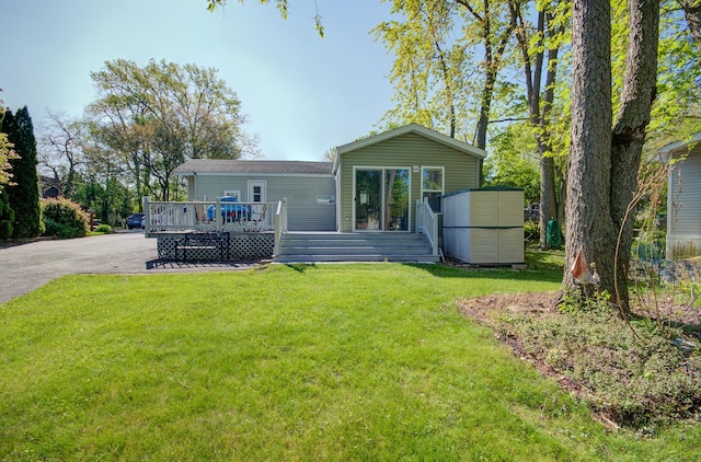 rear view of property featuring a wooden deck, a yard, and driveway