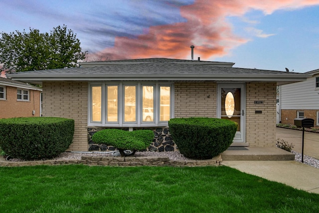 view of front facade with brick siding, a shingled roof, and a front lawn