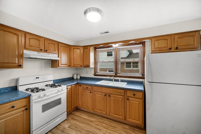 kitchen with visible vents, dark countertops, a sink, under cabinet range hood, and white appliances
