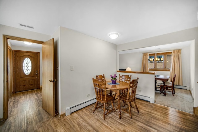 dining area featuring a chandelier, a baseboard heating unit, wood finished floors, and visible vents