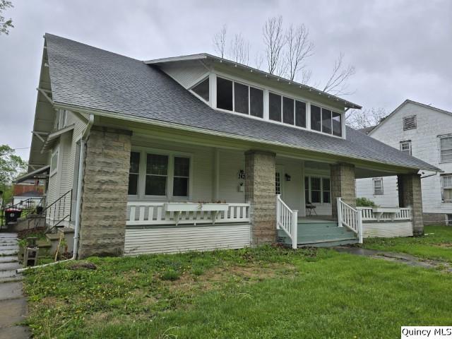 bungalow-style house featuring roof with shingles, a front yard, a porch, and stone siding