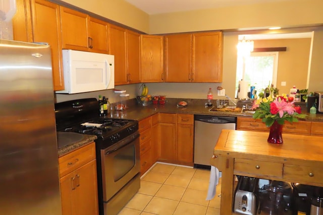 kitchen with stainless steel appliances, light tile patterned flooring, brown cabinets, and dark countertops