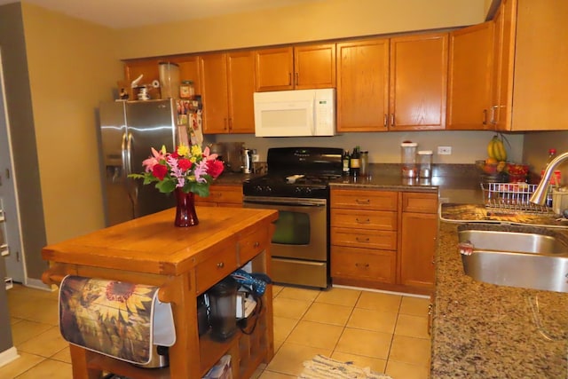 kitchen with stainless steel appliances, a sink, light tile patterned floors, brown cabinets, and light stone counters