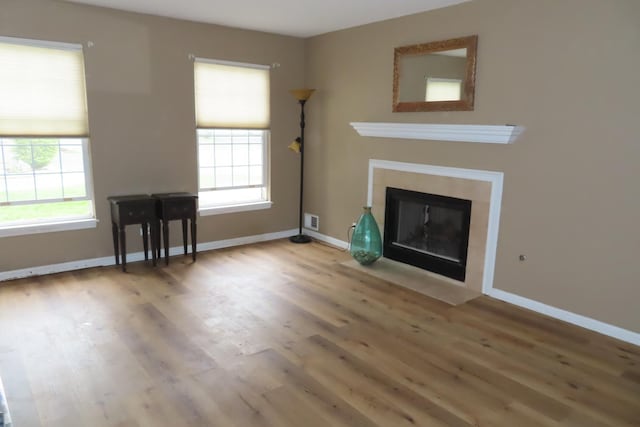 unfurnished living room with wood finished floors, baseboards, and a fireplace with flush hearth