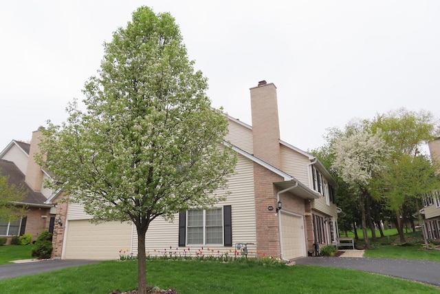 view of front of house with driveway, a front yard, a chimney, a garage, and brick siding