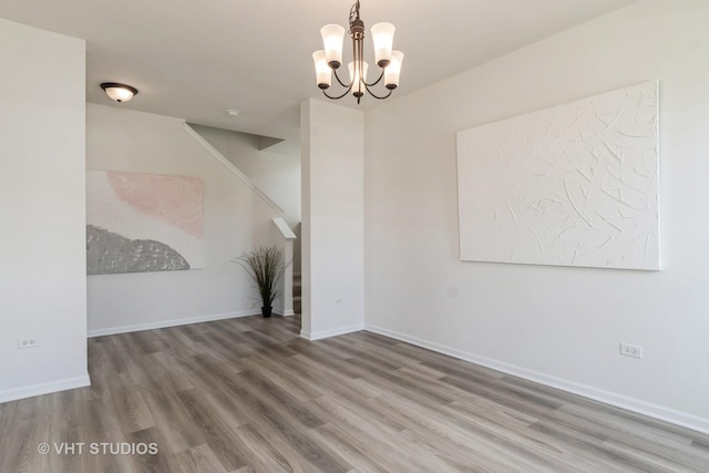 unfurnished room featuring wood finished floors, a chandelier, and baseboards