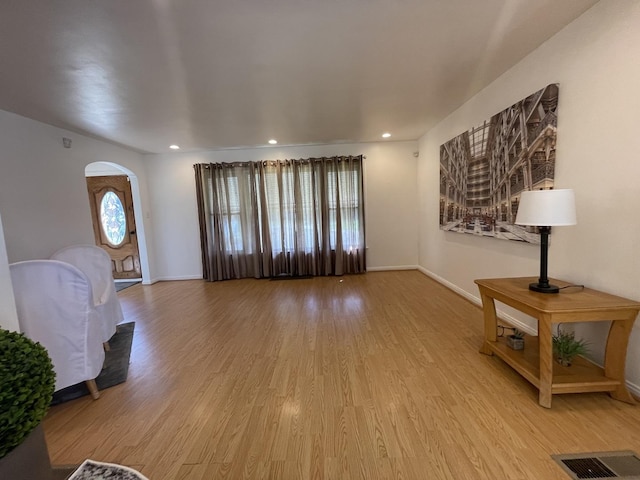 unfurnished living room with light wood-type flooring, baseboards, arched walkways, and recessed lighting