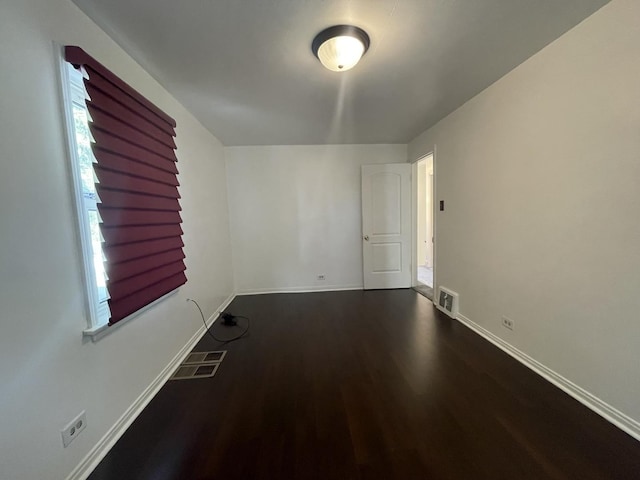 spare room featuring dark wood-type flooring and baseboards