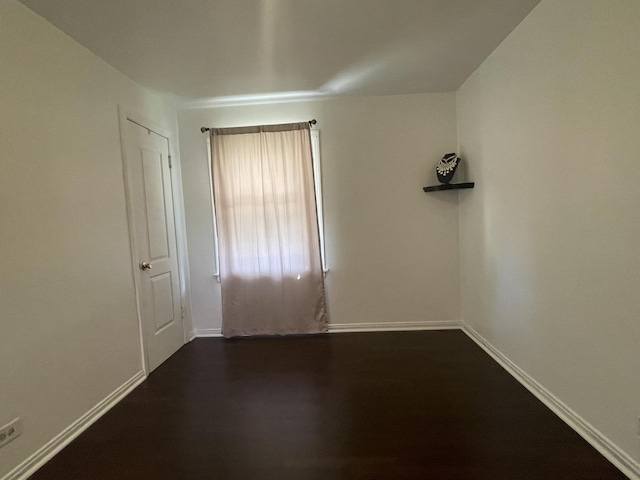 unfurnished room with baseboards and dark wood-style floors
