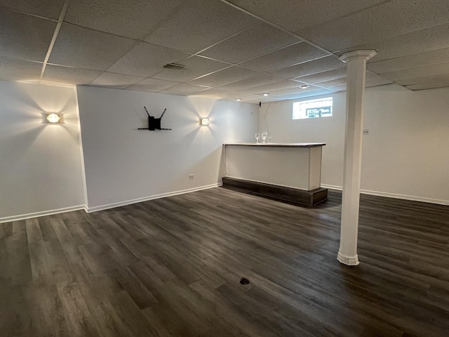 below grade area with dark wood finished floors, bar area, baseboards, and a paneled ceiling