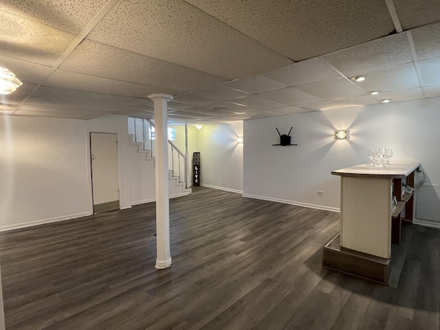 finished below grade area with dark wood-type flooring, baseboards, a paneled ceiling, and stairway