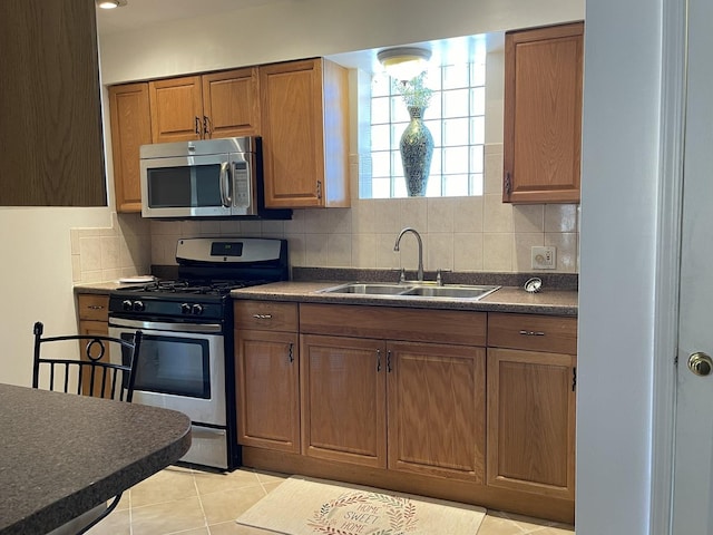 kitchen featuring stainless steel appliances, a sink, dark countertops, tasteful backsplash, and light tile patterned flooring