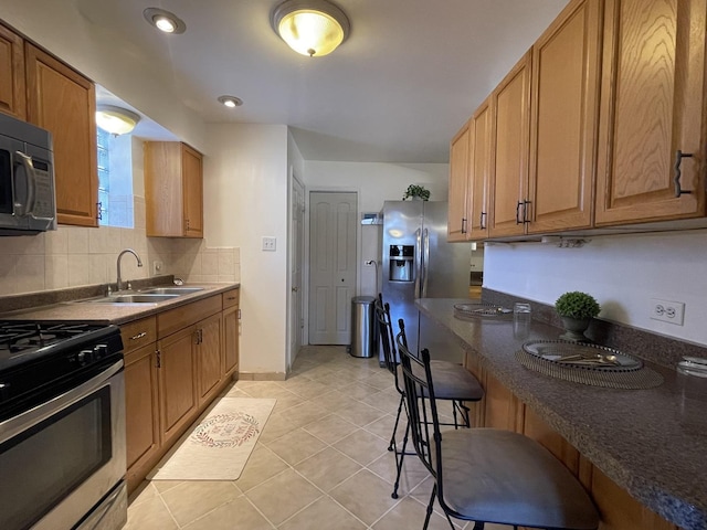 kitchen with appliances with stainless steel finishes, a sink, tasteful backsplash, light tile patterned flooring, and baseboards