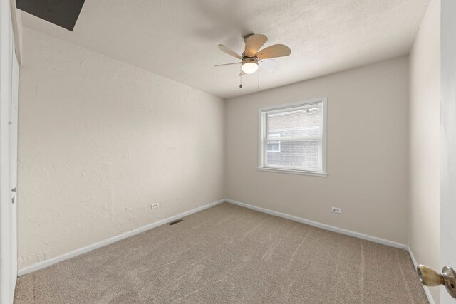 carpeted spare room featuring ceiling fan, baseboards, and a textured wall