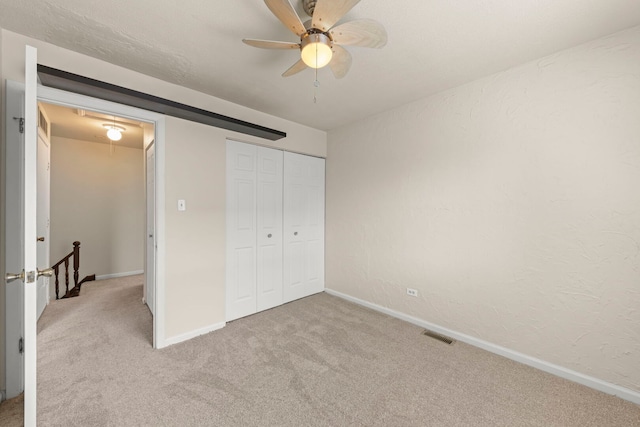 unfurnished bedroom with light colored carpet, baseboards, a closet, a ceiling fan, and a textured wall