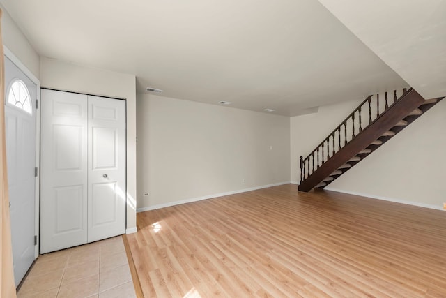 unfurnished living room with stairs, baseboards, and light wood-style floors