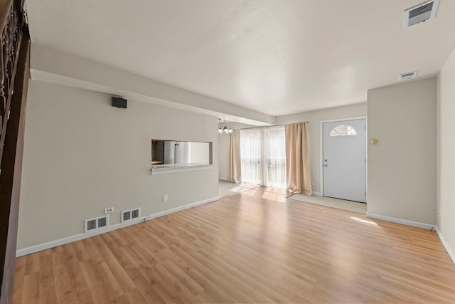 unfurnished living room featuring a chandelier, wood finished floors, and baseboards