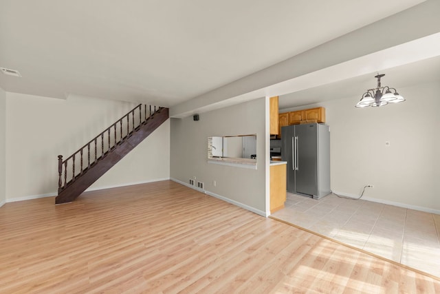 unfurnished living room featuring stairway, baseboards, light wood-type flooring, and a chandelier