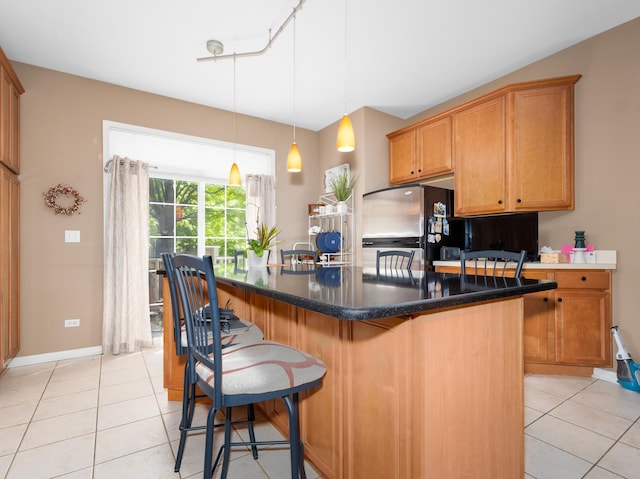 kitchen featuring freestanding refrigerator, baseboards, a breakfast bar area, a center island, and light tile patterned floors