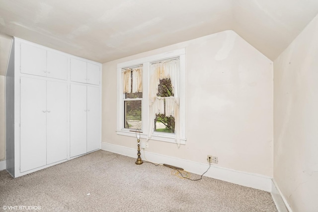 unfurnished bedroom featuring baseboards, a closet, light colored carpet, and vaulted ceiling