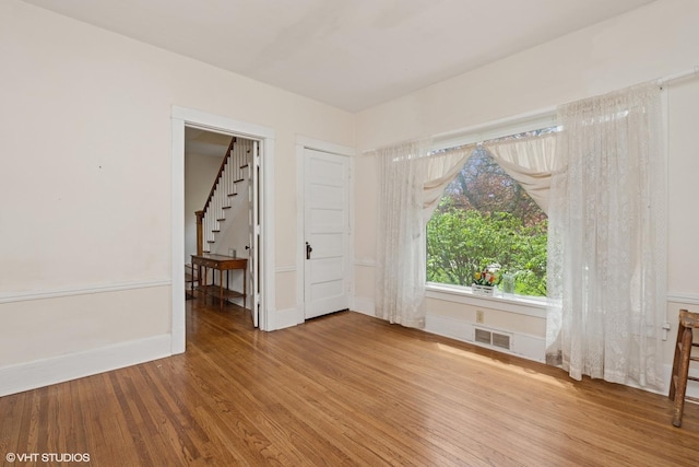 spare room featuring stairway, baseboards, visible vents, and wood finished floors