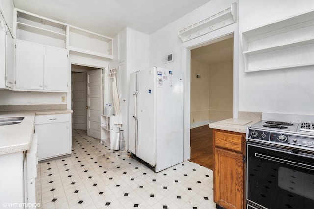 kitchen with freestanding refrigerator, visible vents, a sink, white cabinetry, and electric stove