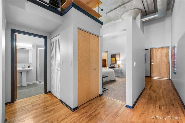 hall featuring baseboards, a sink, light wood finished floors, and a towering ceiling