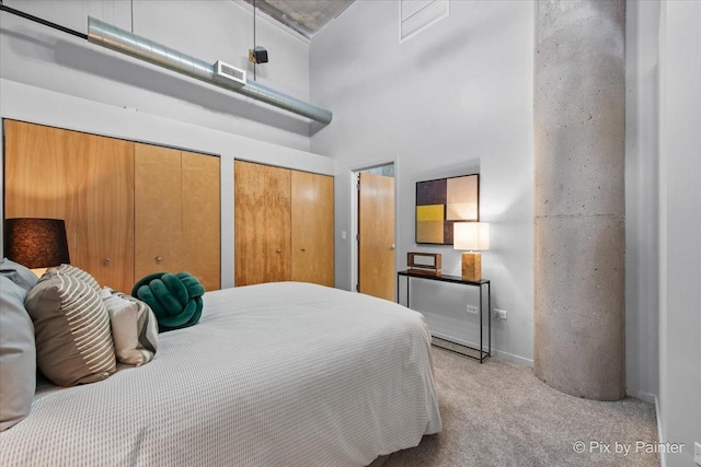 bedroom with light colored carpet, multiple closets, a towering ceiling, and visible vents