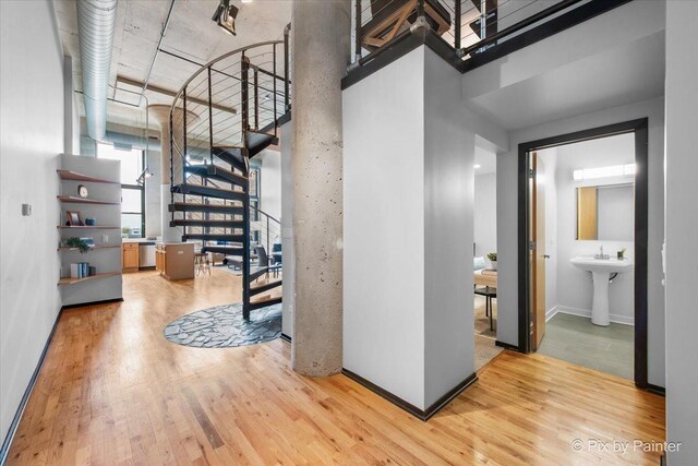 hallway with stairs, a towering ceiling, wood finished floors, baseboards, and a sink