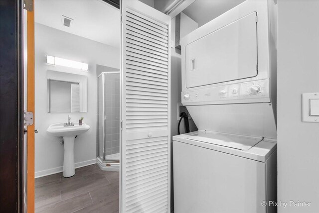 laundry room with laundry area, stacked washer and dryer, visible vents, wood finished floors, and baseboards