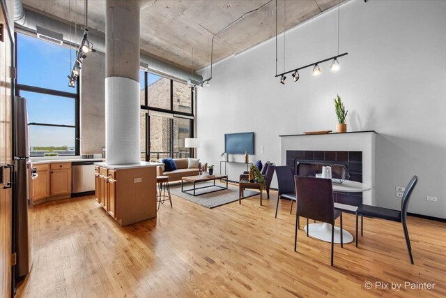 interior space featuring a towering ceiling, a tiled fireplace, light wood-type flooring, rail lighting, and ornate columns