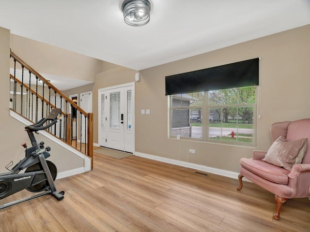 foyer entrance featuring baseboards, stairs, light wood-style flooring, and visible vents