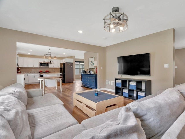 living area with baseboards, light wood-style floors, a chandelier, and recessed lighting