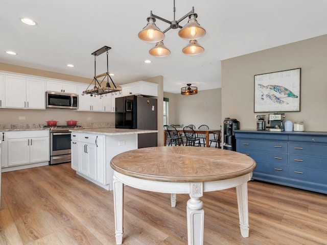 kitchen featuring white cabinets, appliances with stainless steel finishes, hanging light fixtures, and light wood finished floors