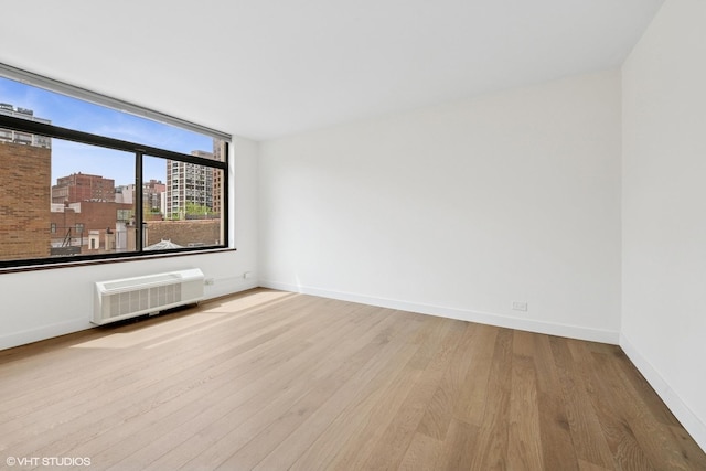 spare room with baseboards, an AC wall unit, wood finished floors, and a view of city