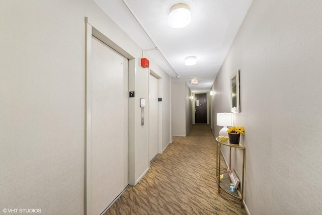 hall with baseboards, elevator, and light colored carpet