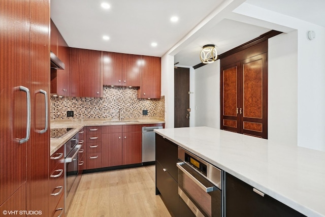 kitchen with a sink, light wood finished floors, light countertops, stainless steel appliances, and decorative backsplash