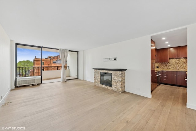 unfurnished living room with a sink, a stone fireplace, light wood-style flooring, recessed lighting, and baseboards