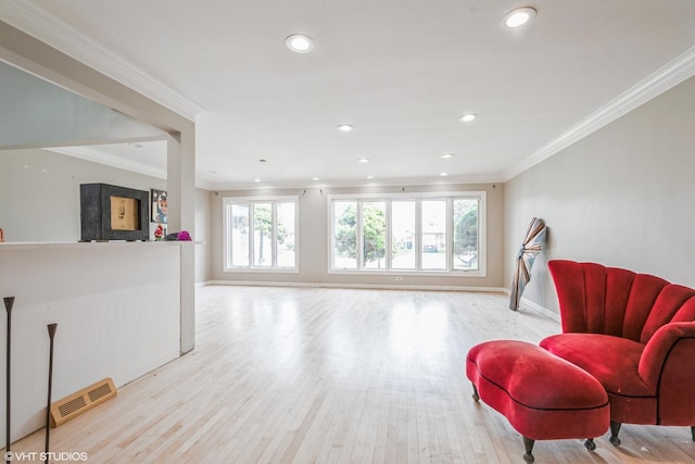 living area featuring crown molding, visible vents, a wealth of natural light, and light wood-style floors