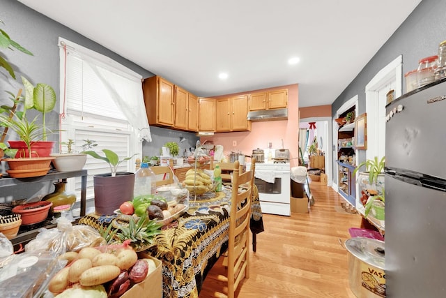 kitchen featuring light brown cabinetry, freestanding refrigerator, under cabinet range hood, light wood-style flooring, and white stove
