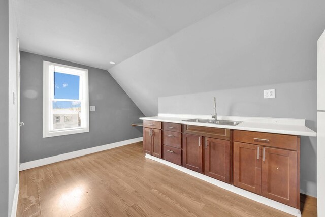 bar with light wood-type flooring, a sink, baseboards, and vaulted ceiling