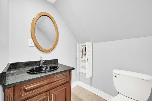 half bath with vanity, tile patterned floors, vaulted ceiling, and toilet