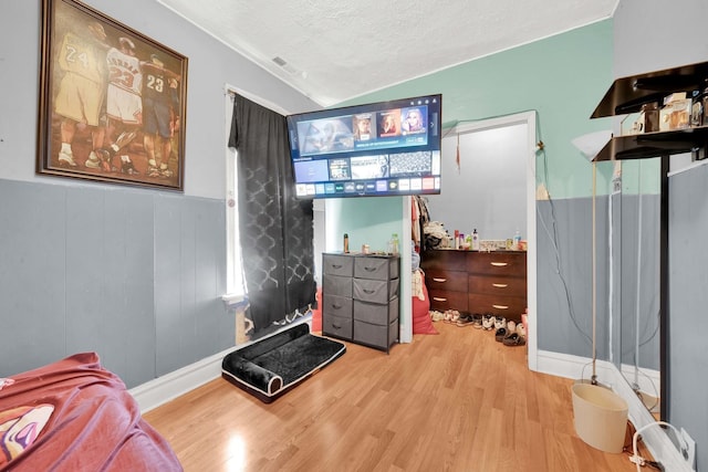 bedroom with visible vents, wainscoting, wood finished floors, a textured ceiling, and vaulted ceiling