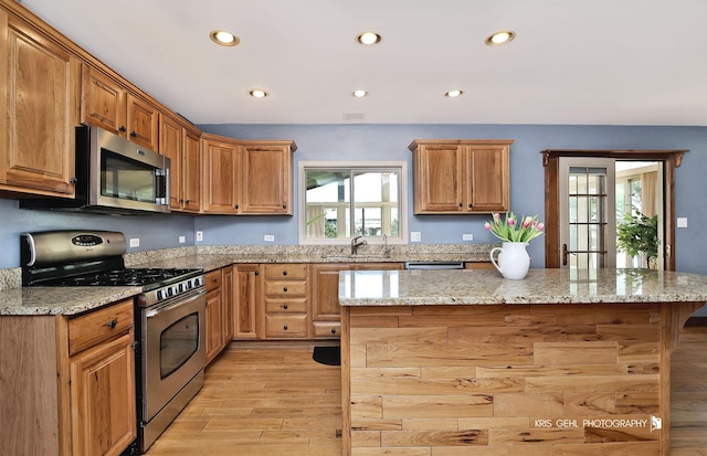 kitchen with stainless steel appliances, a sink, light wood finished floors, recessed lighting, and a center island